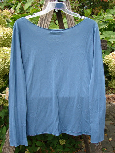 Barclay NWT Batiste Raw Edge Layering Tee Unpainted Blue Bird Size 1, featuring long sleeves, raw cut neckline, rolled edgings, and tapered shape, hung on a clear hanger against a floral background.