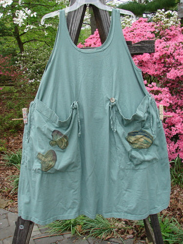 Vintage 1998 Harvest Pinafore Organic Garden Kale Size 1, showcasing a green apron with oversized painted pockets on a wooden pole. Reflecting BlueFishFinder's ethos of unique, creative fashion for all women.