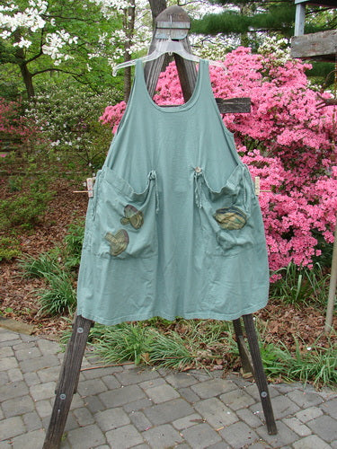 Vintage 1998 Harvest Pinafore Organic Garden Kale Size 1 displayed on a wooden stand. Features oversized painted pockets, sectional panels, original buttons, and a unique reversible design. Reflects BlueFishFinder's ethos of creative individuality.