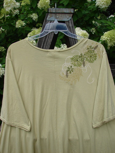 Image alt text: Barclay High Low Top Dandelion Trail Dawn Size 2: Swingy shirt on a wooden stand, made from organic cotton. Deeper rounded neckline, varying upward front hemline, center rear vertical seam.