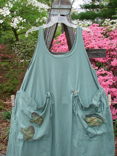 Vintage 1998 Harvest Pinafore Organic Garden Kale Size 1 displayed on a wooden rack. Features include oversized painted pockets, sectional panels, original buttons, and thin shoulder straps. Reflects BlueFishFinder's ethos of creative expression through unique vintage clothing.