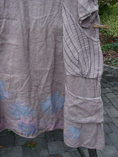 Barclay NWT Linen Calotype Stack Pocket Dress Grow Garden Oriel Size 0: Light-tan smock-style dress with blue floral hem, three-quarter sleeves, empire waist, and unique pocket design, hanging outdoors.