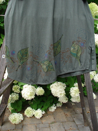 Barclay Double Pocket Lace Twinkle Top in Deep Forest, Size 2. A cloth on a rack with grey leaves, white flowers, and a wood bench.