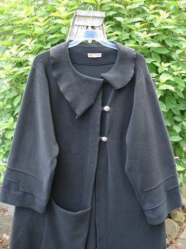 Barclay Celtic Moss Asymmetrical Collar Coat in black displayed on a hanger, showcasing its unique collar, button closure, varying hemline, and distinct bell sleeves, reflecting BlueFishFinder's vintage, creative fashion ethos.