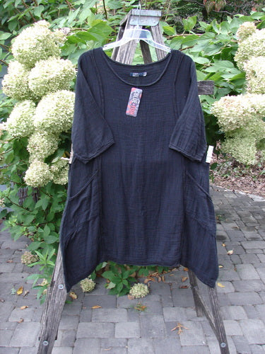 Barclay NWT Gauze Daily Pocket Dress Unpainted Jet Black Size 0 displayed on a wooden stepladder outdoors, highlighting its elbow-length sleeves, A-line shape, and softly rolled edges amidst a natural garden setting.