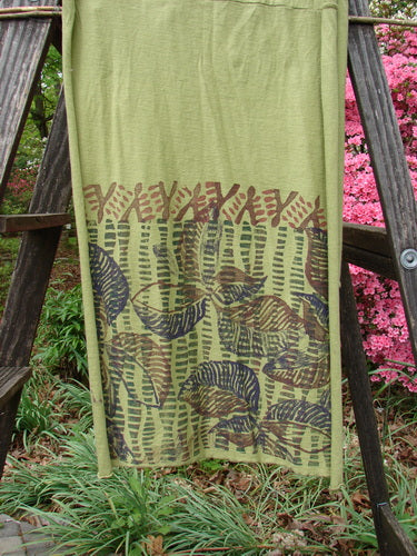 Barclay Sectional Wrap Scarf featuring Forest Leaf design in Peapod. Organic cotton, cozy with rolled edges. Versatile as shawl or waist wrap. Measures 20W x 75L. Image: towel on ladder, plant.