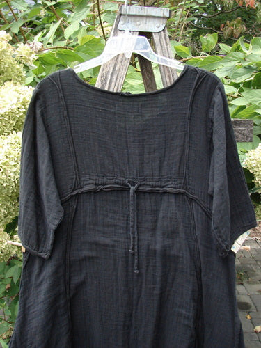 Barclay NWT Gauze Daily Pocket Dress Unpainted Jet Black Size 0, featuring rolled sleeves and edges, drawstring under-bust detail, and unique vertical seams, elegantly draped on a rustic ladder.