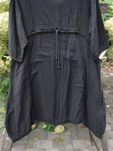 Barclay NWT Gauze Daily Pocket Dress Unpainted Jet Black Size 0 draped over a wooden garden chair, featuring three-quarter sleeves, drawstring waist, flared hem, and rolled edges, embodying BlueFishFinder's unique vintage style.