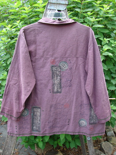 Barclay Hemp Cotton Metal Button Workshirt features contrasting stitchery, full metal buttons, a shirttail hemline, and Asian script detail. Displayed on a pole, highlighting its unique design and craftsmanship.