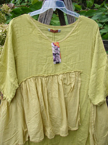 Barclay NWT Gauze Batiste Petal Urchin Flounce Dress Unpainted Citron Size 1, featuring a crinkled texture, scooped neckline, elbow-length sleeves, and gathered bodice, displayed on a clear hanger.