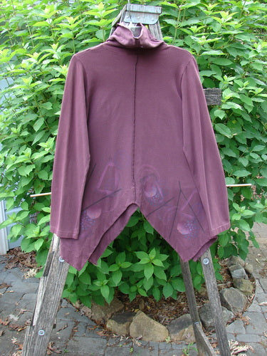 Barclay Cotton Lycra Symmetrical Turtleneck Top Galaxy Deep Burgundy Size 0 features a unique turtleneck, varying hemline, and exterior stitching. The top is displayed on a wooden post alongside purple outerwear.
