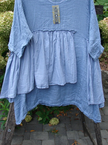 Barclay NWT Gauze Batiste Petal Urchin Flounce Dress in Dusty Sky, featuring a tiered, gathered front and three-quarter sleeves, displayed outdoors with a tag attached, showcasing its unique flowing design.