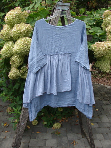 Barclay NWT Gauze Batiste Petal Urchin Flounce Dress Unpainted Dusty Sky Size 1, showcased on a hanger, features a scooped neckline, elbow-length sleeves, and an asymmetric, tiered hem with a whimsical flair.