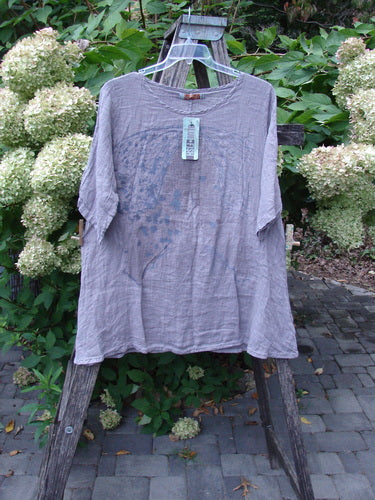 Barclay NWT Linen Simple Tunic Top in Opal Mauve hangs on a ladder, showcasing its flowy A-line shape, rounded neckline, and three-quarter sleeves against a garden backdrop.