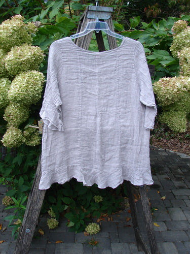 Barclay NWT Gauze Sectional Bias Flounce Top Unpainted Rice Paper Pink Size 1, features a lightweight linen with elbow-length ruffled sleeves, gently wavy hem, and A-line shape, displayed outdoors.