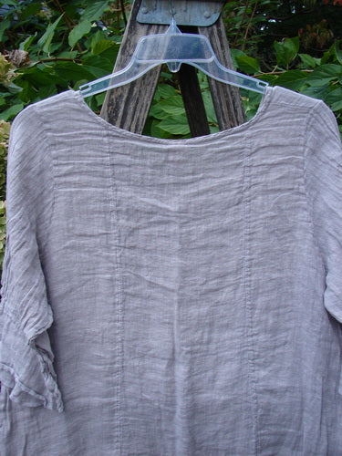 Barclay NWT Gauze Sectional Bias Flounce Top in Rice Paper Pink, featuring a scooped neckline and three-quarter sleeves with petal accents, elegantly draped on a wooden structure.