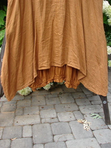 Image alt text: Barclay Linen Open Front Drawcord Hem Jumper Garden Squash Size 2 - A brown dress with interesting layered cross over front and elastic gathered hemline, made from linen and batiste, on a brick patio.