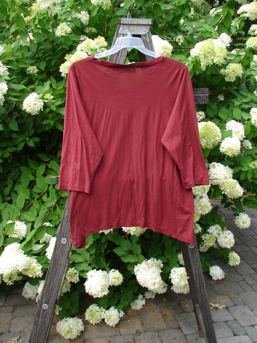 A red shirt with 3/4 length sleeves and a soft V-shaped neckline on a swinger, surrounded by white flowers on a bush.
