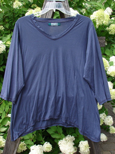 Image: A blue shirt on a hanger. 

Alt text: Barclay Tissue Raglan V Neck Layering Top Unpainted Navy Sky Size 2 - A lightweight blue shirt with 3/4 length sleeves and a soft V-shaped neckline on a hanger.