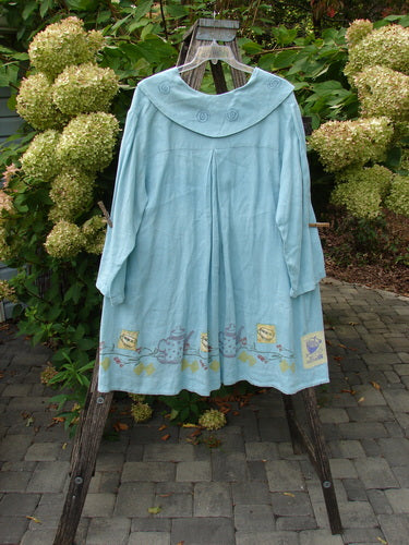 1999 Linen Breeze Jacket Tea & Cherries Spring OSFA: This pastel-blue smock-style coat features a rounded collar with spiral embroidery, whimsical animal appliqué, and exterior oversized pockets, embodying Blue Fish's creative, vintage-inspired style.