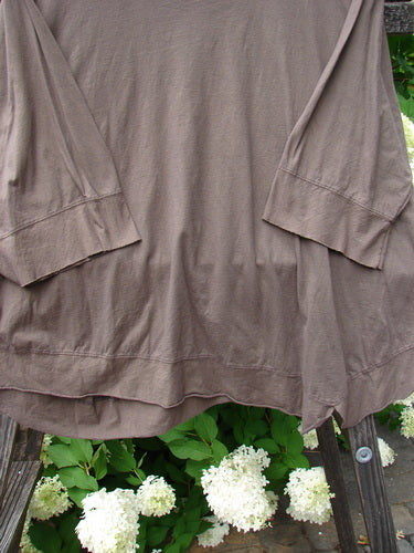 Barclay NWT Angle Flutter Bottom Top in Deep Sand, featuring a brown shirt on a wooden ladder, white flowers, and green leaves.