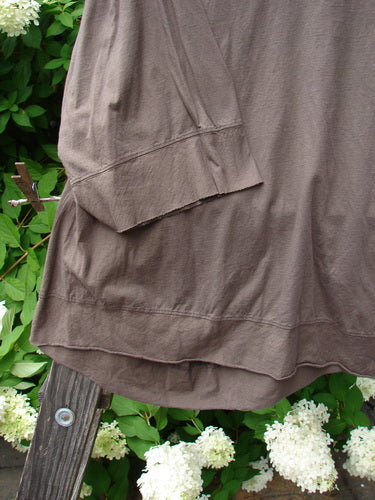 Barclay NWT Angle Flutter Bottom Top in Deep Sand, a close-up of a brown shirt with a small flutter accent, angled hemline, and raw cut hem.