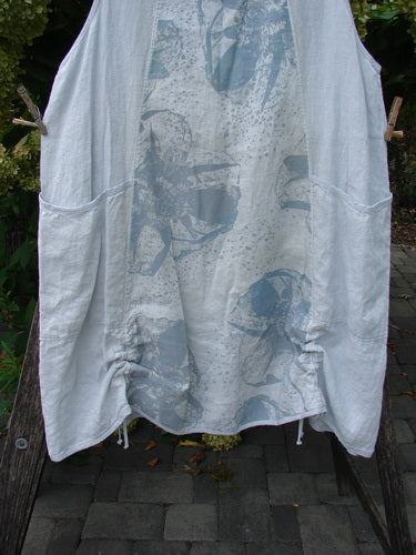 Barclay NWT Linen Image Pinafore Pocket Overpiece in Floral Burst Dew, displayed outdoors, featuring a sleeveless design, two large hip pockets, and abstract human figure prints, hanging on a clothesline.