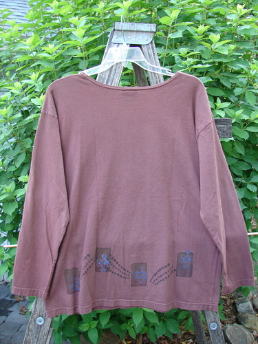 Barclay Long Sleeved Studio Tee Celtic Wind Loam Size 0 displayed on a wooden swing, showcasing its straight boxy shape, thinner flattened neckline, and whimsical character, made from mid-weight organic cotton.