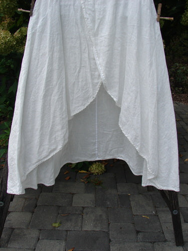 Barclay NWT Linen Tulip Midlayer Overpiece Unpainted White Size 0, showcasing layered panels with a curved empire waist, elegantly draped on a wooden frame against a stone-paved backdrop.