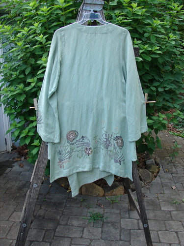 Barclay Viscose Long Ribbon Side Tie Jacket, featuring a single ribbon closure and painted hemline, displayed on a clothes rack, showcasing the garment's elegant design and unique sway.