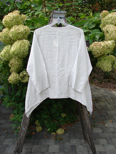 Barclay NWT Linen Basque Cardigan Unpainted Dove Size 0 displayed on a wooden hanger outside, highlighting its loose fit, super deep V neckline, and oversized shell buttons amidst a garden setting.