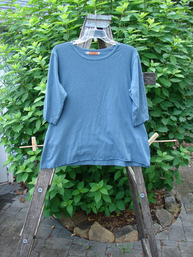 Barclay Slub Three Quarter Sleeved Cafe Tee Unpainted Tealen Size 1 displayed casually on a wooden rack, showcasing its rounded neckline, slight line flare, three-quarter sleeves, and curly edgings.