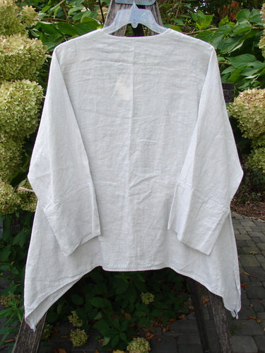Barclay NWT Linen Basque Cardigan Unpainted Dove Size 0: A loose-fitting white linen tunic with long sleeves, deep V-neckline, oversized shell buttons, and dippy sides, hangs outdoors against green foliage.