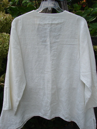 Barclay NWT Linen Basque Cardigan Unpainted White Size 0, featuring a deep V neckline, dippy sides, and oversized shell buttons, displayed on a hanger with a leafy garden backdrop.