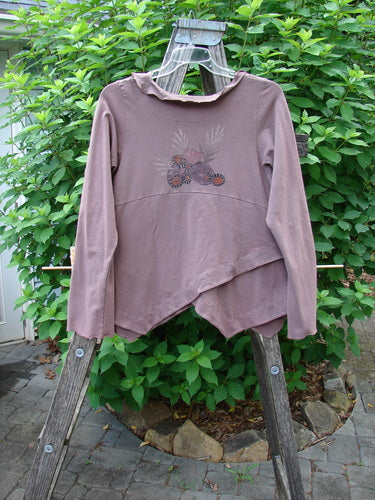 Barclay Cotton Lycra Tiny Button Cross Over Top in Galaxy Dusty Burgundy, featuring a unique wrap front, flowing batiste collar, alternating hemline, and detailed button loops, displayed on a clothes rack.