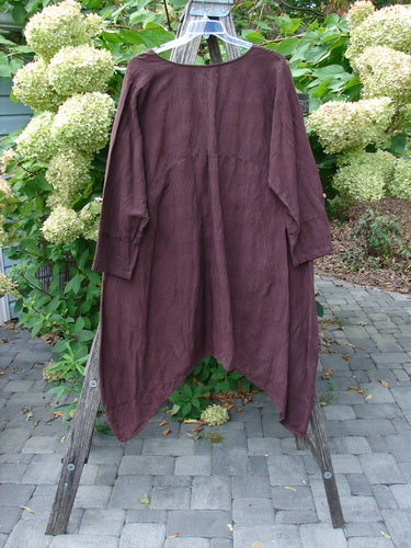 Barclay NWT Linen Geoides Pocket Duster Unpainted in Armagnac Red Plum, loose-fitting with asymmetric drapey hem, hanging on a wooden ladder stand outdoors, showcasing a natural-fiber blend texture.