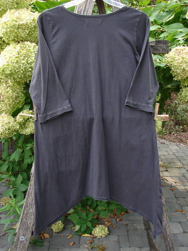 Barclay NWT Sunny Day Pocket Tunic Dress Flutter Bamboo Steel Meteorite Size 1, features a charcoal-gray, three-quarter-sleeve design with an asymmetrical draped hem, hanging elegantly amidst lush foliage.
