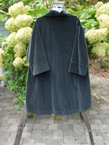 Barclay NWT Velvet Opera Pocket Coat, Blue Black, Size 0, displayed on a wooden stand. The coat's luxurious, heavier-weight cotton velvet drapes elegantly against a natural garden backdrop.