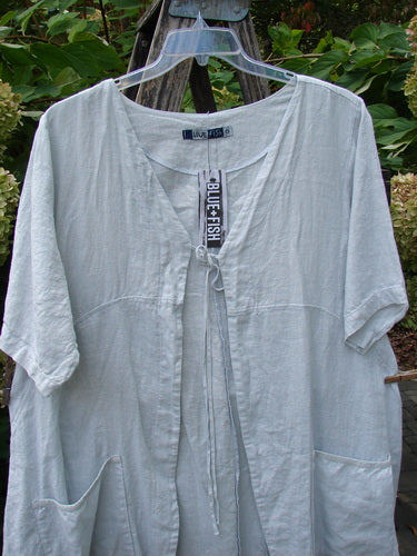 Barclay NWT Linen Contrast Tie Pocket Cardigan, a relaxed, off-white tunic with a V-neck, short sleeves, and front pockets, hangs outdoors, featuring a Blue Fish tag. Perfect for spring layering.