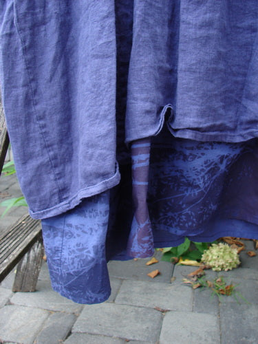 Barclay NWT Linen Process Two Story Dress Mum Ultra Violet Size 0 drapes over a wooden bench, showcasing layered lightweight linen with a patterned percale underskirt, amidst natural outdoor elements.