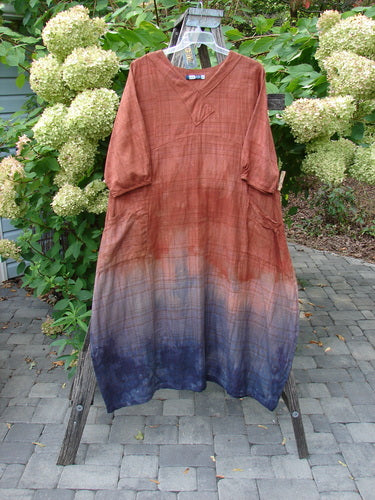 Barclay NWT Flannel Cross Over Blue Moon Pocket Dress in Terra Ombre Plaid, loose-fitting with three-quarter sleeves and a round neckline, shown on a wooden ladder outdoors.