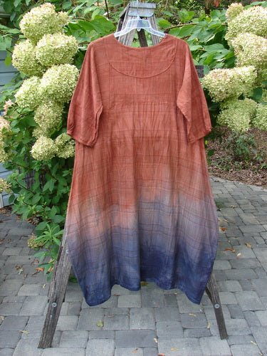 Barclay NWT Flannel Cross Over Blue Moon Pocket Dress Terra Ombre Plaid Size 0 displayed on a wooden ladder; lightweight, long-line with gradient from rusty brown to deep indigo, surrounded by foliage.