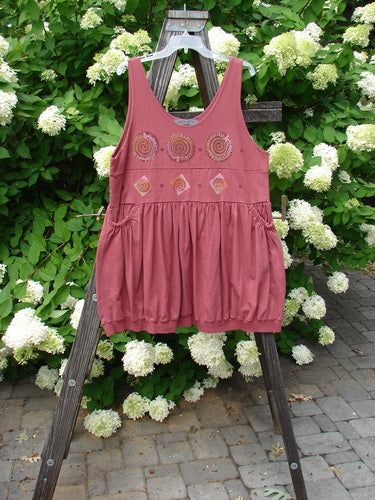 1996 Amusement Jumper Circle Track Ember Size 1: A pink dress with spirals on it, hanging on a wooden ladder.