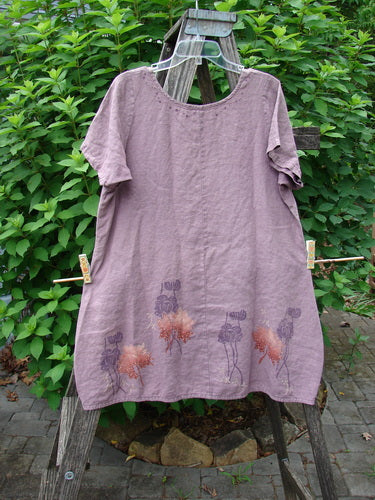 Barclay Linen Urchin Dress Necklace Leaf Dusty Plum Size 0 displayed on a wooden stand, showcasing a flowing hemline and intricate floral pattern, embodies vintage Blue Fish Clothing's artistic style.
