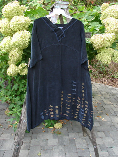 Barclay NWT Cupro Cross Over Urchin Dress in Primitive Metallic Black features elbow-length sleeves and a notched V-neckline with tan geometric motifs on the hem, displayed against a natural backdrop.