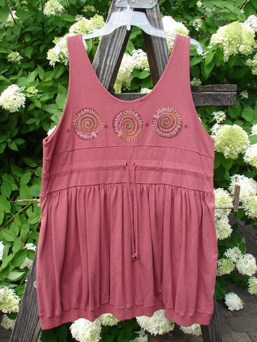 1996 Amusement Jumper Circle Track Ember Size 1: A pink dress with spirals on it, featuring a draw cord back, elastic front pockets, double layered bodice, ribbed hemline, and a colorful circle track theme paint.