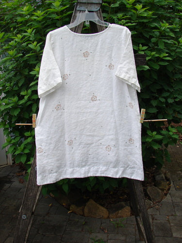 Barclay Linen Shirt Tail Top Circle Center Daisy Chain White Size 0 displayed outdoors, showcasing its rounded neckline, vented shirt tail hemline, and distinctive daisy border design, embodying BlueFishFinder's vintage, creative style.