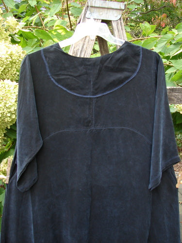 Barclay NWT Cupro Cross Over Urchin Dress in Primitive Metallic Black hangs on a white hanger, showcasing its loose fit, rounded neckline, and mid-length sleeves, against a natural backdrop.