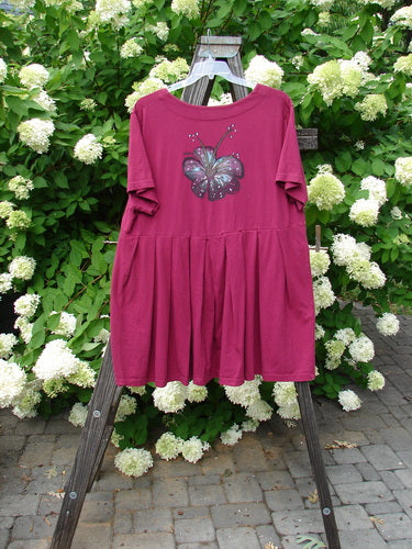 Barclay Boxcar Dress with Rear Blossom in Cranberry, Size 2. A pink dress with a butterfly on it. Beautifully squared double paneled deeper neckline, empire waist seam, wide full pleats, and a forever lower flair. Bust 50, waist 52, hips 58, hem circumference 120, length 37 inches.