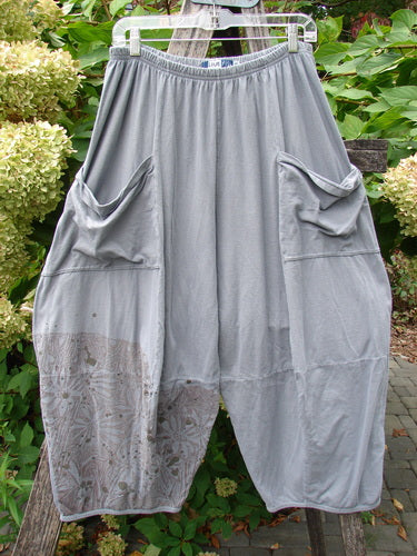Barclay Crop Two Pocket 4 Square Pant Spin Flower Grey Green Size 0 displayed, featuring loose-fitting design, elastic waistband, oversized side pockets, and a subtle pattern on the lower leg against garden foliage.